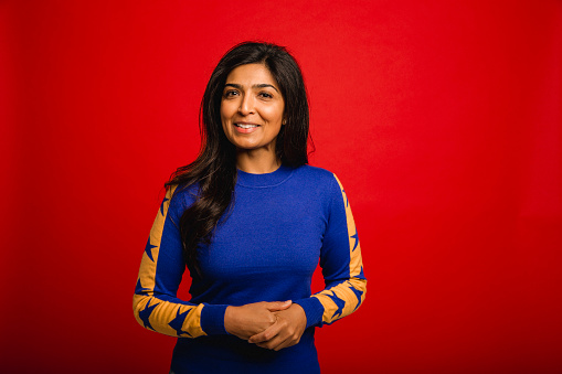 Portrait of a mid adult woman standing infront of a red studio background.